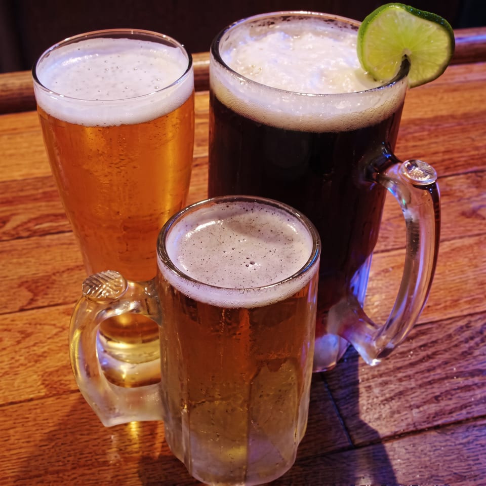 Three glasses of beer, one dark with a lime, on a wooden table.