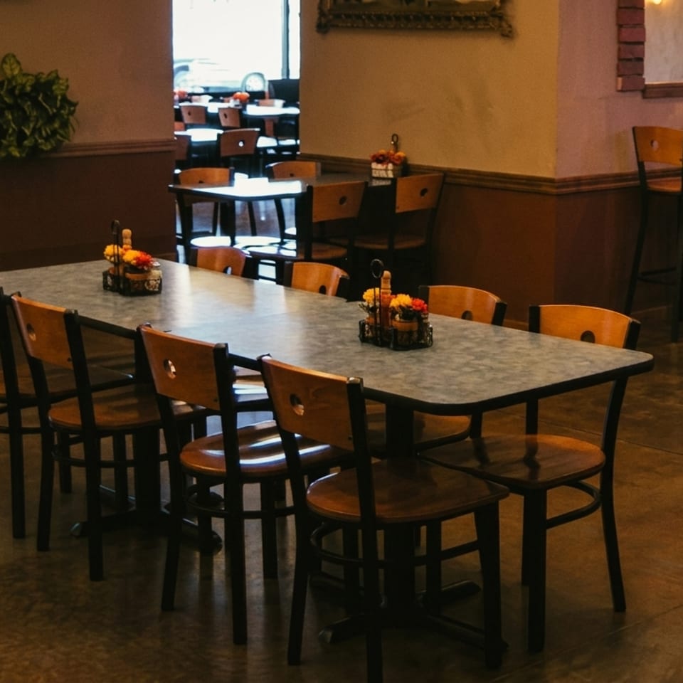 Restaurant interior with long dining tables, wooden chairs, and high-top tables in the background.