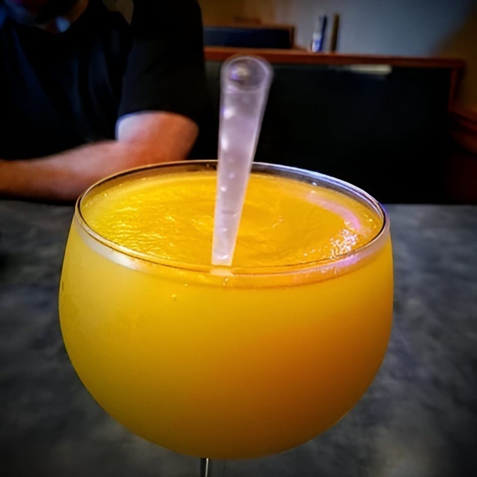 A large goblet of bright yellow frozen drink with a straw, a person in the background.